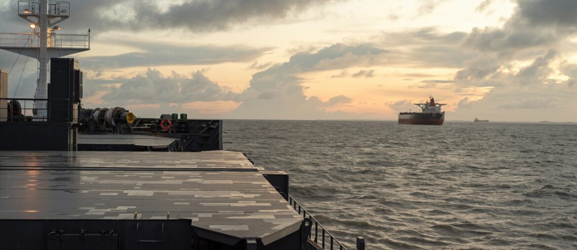 Bulk carrier hatch covers with another cargo ship anchored at dusk