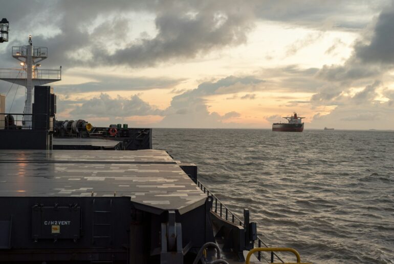 Bulk carrier hatch covers with another cargo ship anchored at dusk
